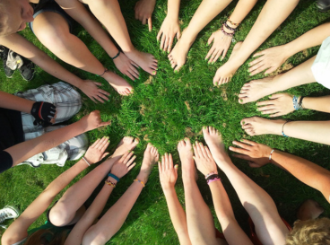 Cercle formé par des mains et pieds de jeunes posés sur l’herbe, symbolisant l’unité et la coopération